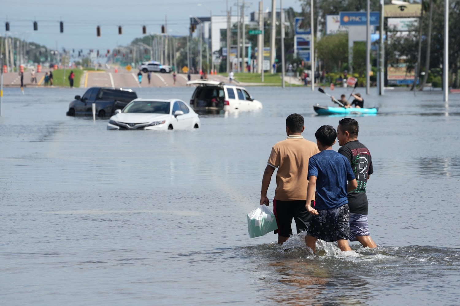 Kids walk past vehicles flooded in the water as the streets of the Southeast Seminole Heights section of Tampa due to Hurricane Milton on October 10, 2024 in Florida. Hurricane Milton tore a coast-to-coast path of destruction across the US state of Florida, whipping up a spate of deadly tornadoes that left at least four people dead, but avoiding the catastrophic devastation officials had feared. (Photo by Bryan R. SMITH / AFP) (Photo by BRYAN R. SMITH/AFP via Getty Images)