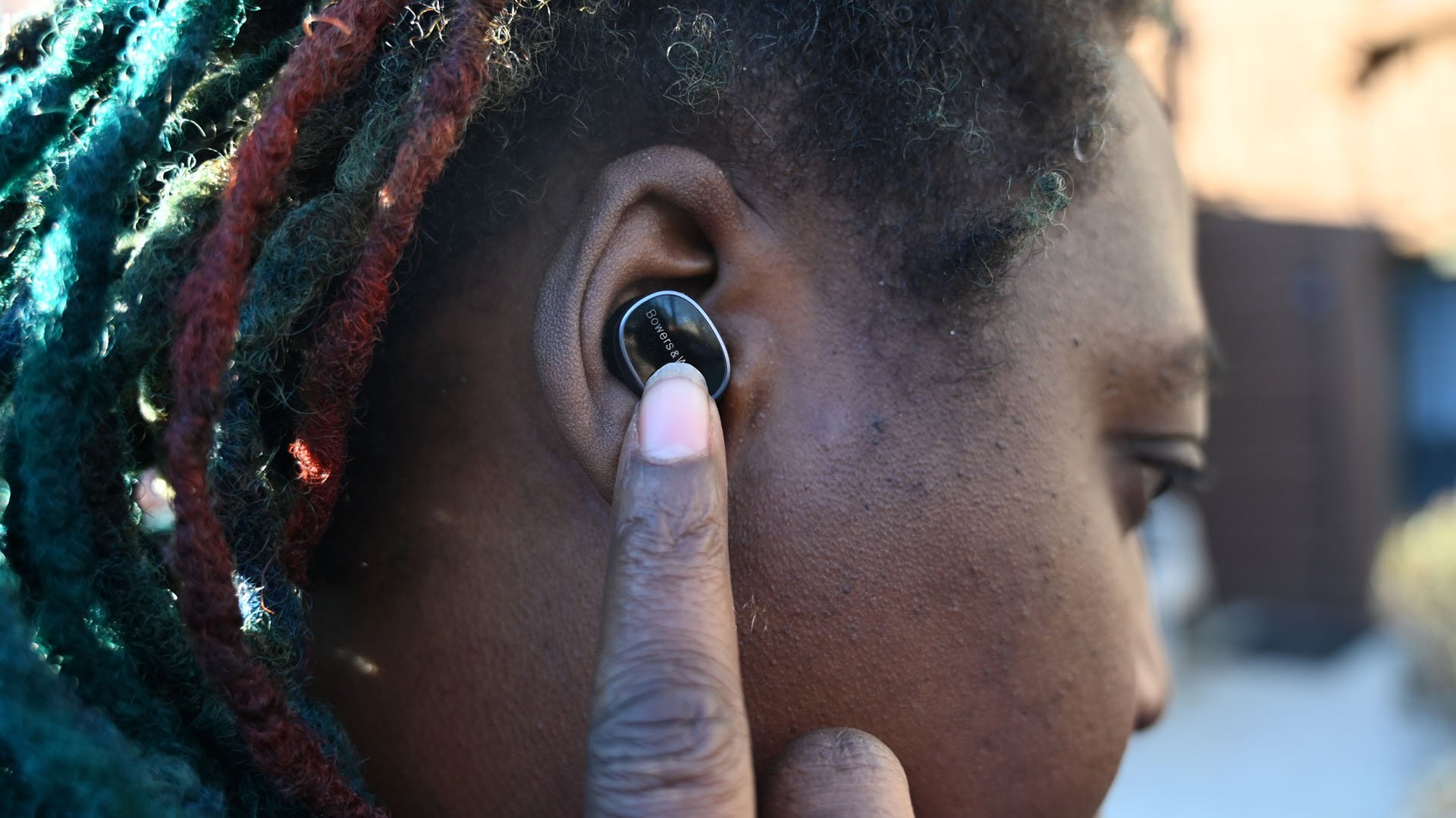 Shot of African-American woman wearing Bowers & Wilkins Pi8 earbuds using tap control