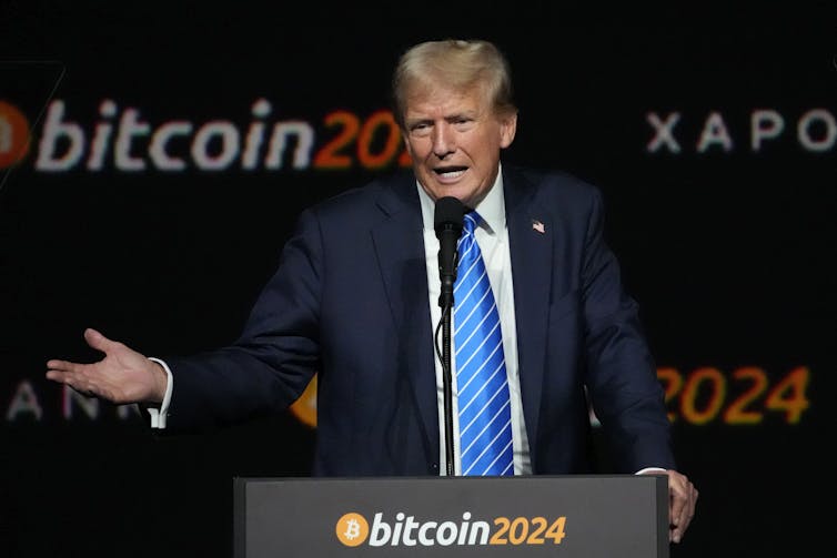 A man in a business suit stands at a lectern and gestures.