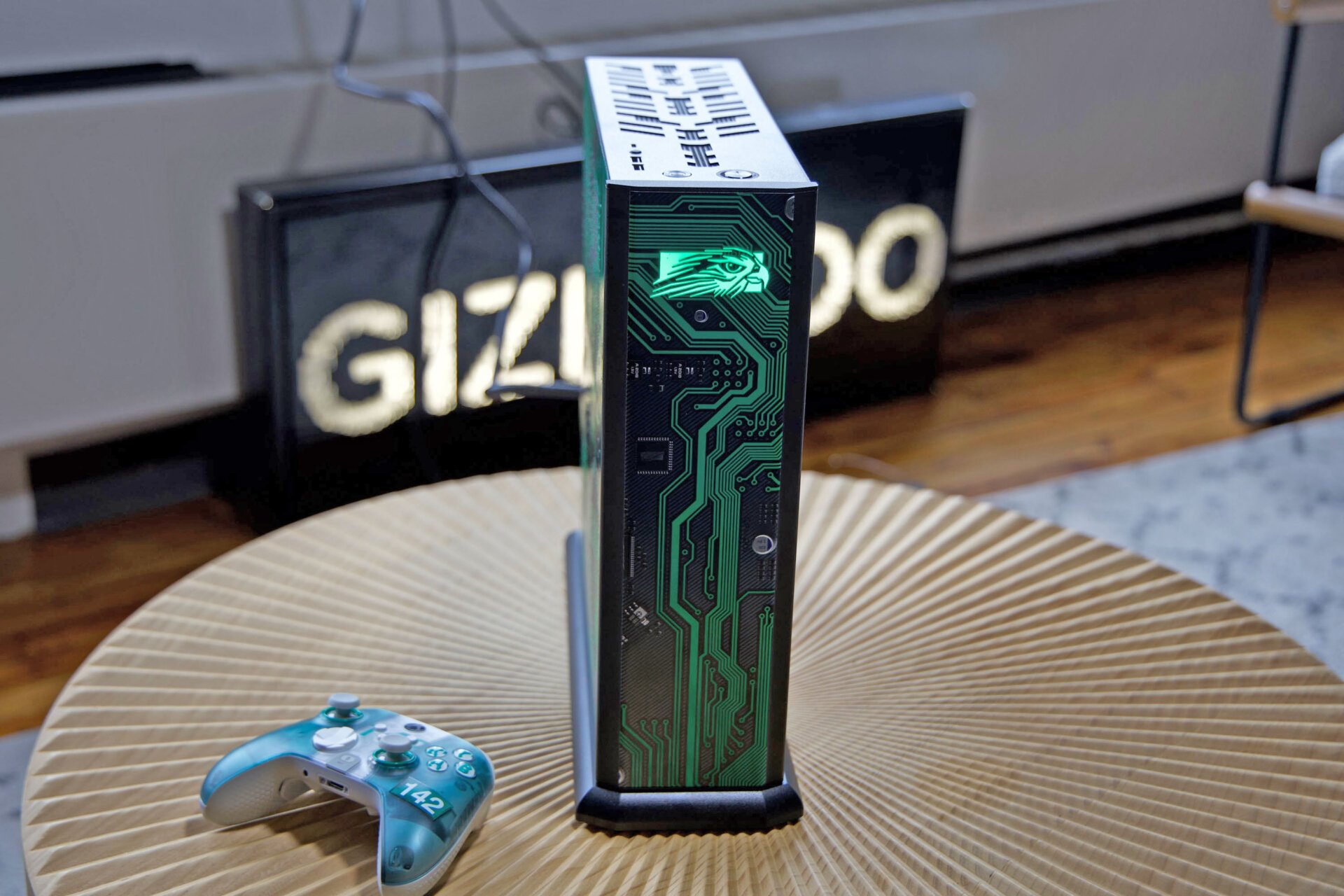 Front shot of Northwest Falcon Tiki with green and white Xbox Scuf controller on wooden table with Gizmodo sign in the back