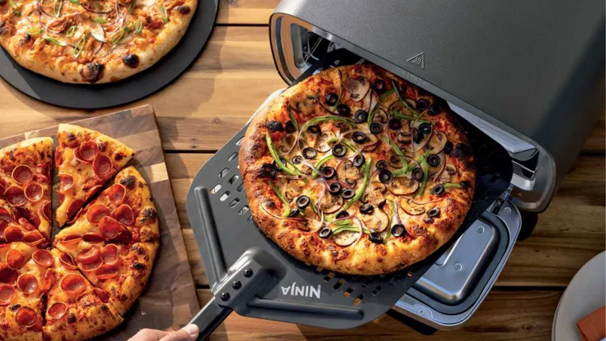 Overhead view of pizza being removed from the oven, with other pizzas on the table