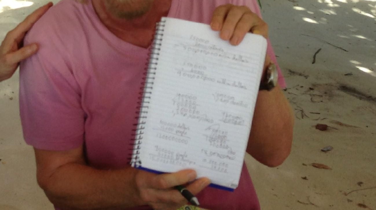 A zoomed in perspective on a photo of Richard Branson holding up a notebook while seated near Jeffrey Epstein.