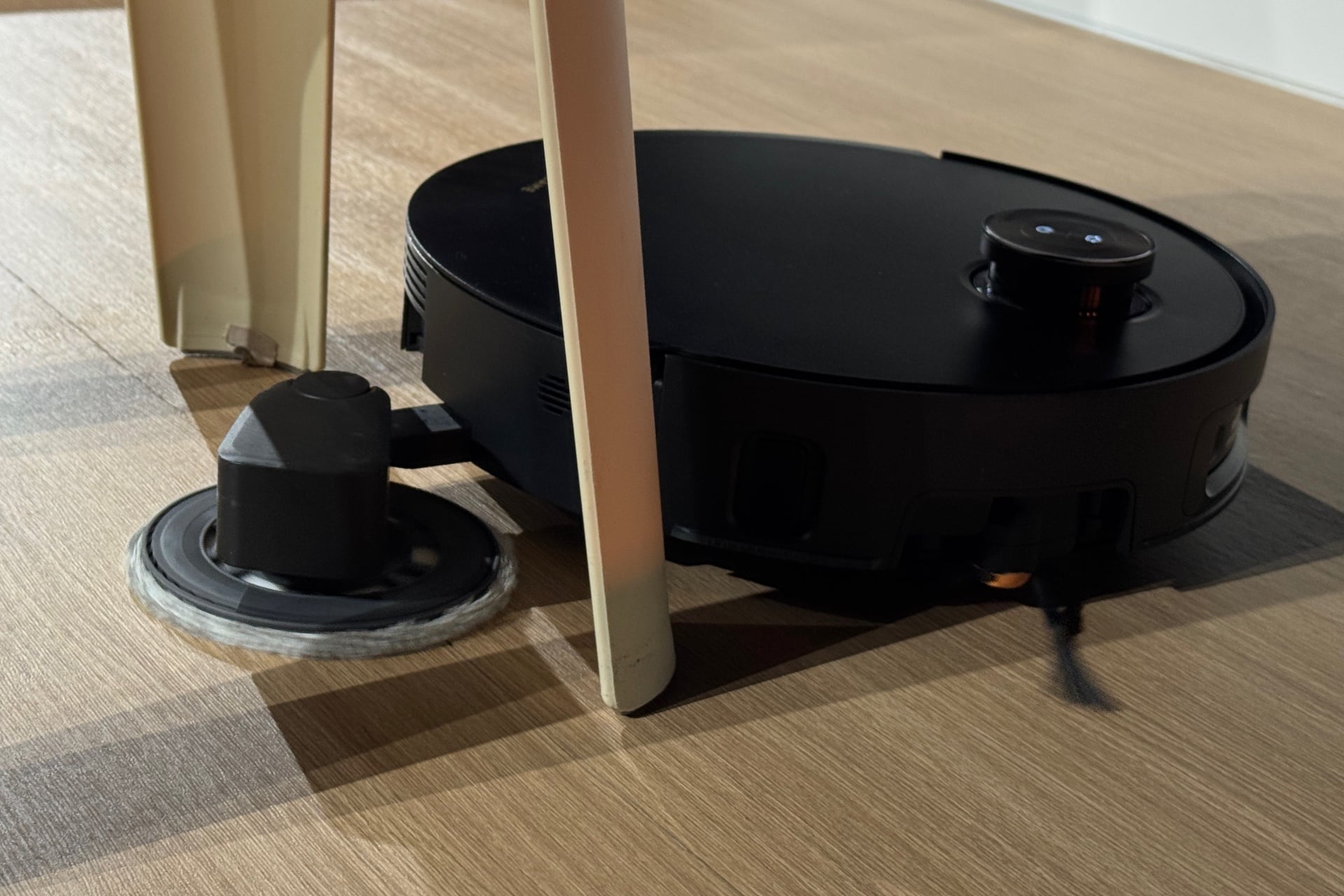 A black robot vacuum extends its mop pad between two stool legs